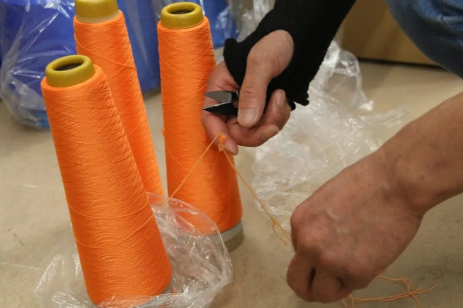 オレンジ色の糸のコーンと、糸を手作業で扱う手元